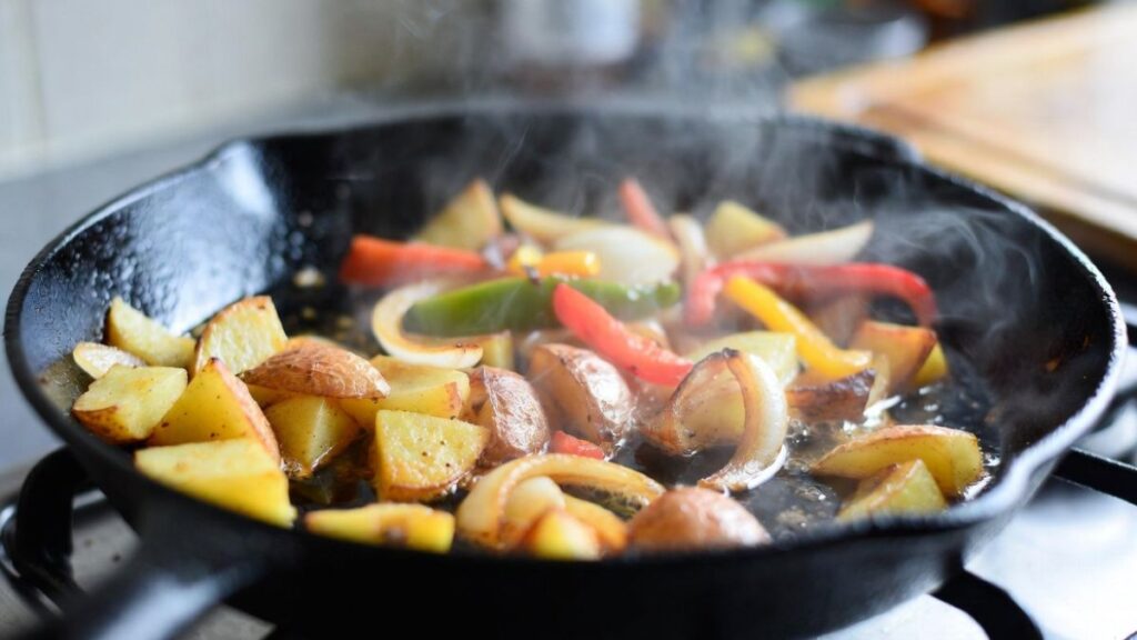 Potatoes, onions, and bell peppers cooking in a skillet