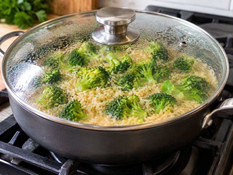 Chicken rice simmering with broccoli in a covered skillet