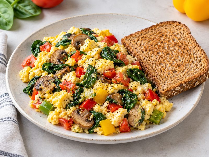 Vegetable egg scramble with spinach peppers tomatoes and whole grain toast