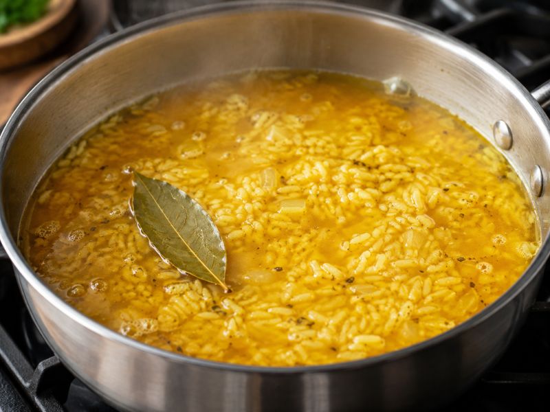 yellow rice cooking with broth and bay leaf