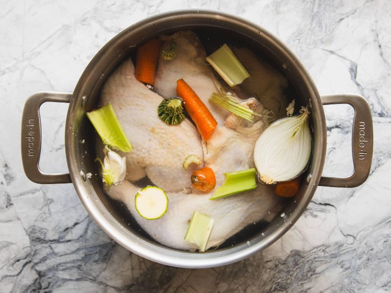 Chicken bones and fresh vegetables added to a stockpot with water and herbs