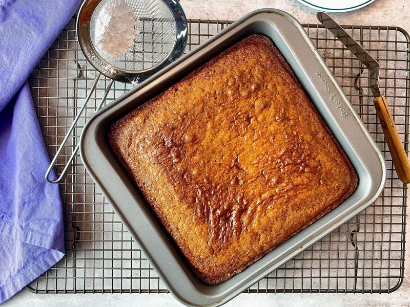 Freshly baked golden brown applesauce cake cooling in its baking pan on a wire rack