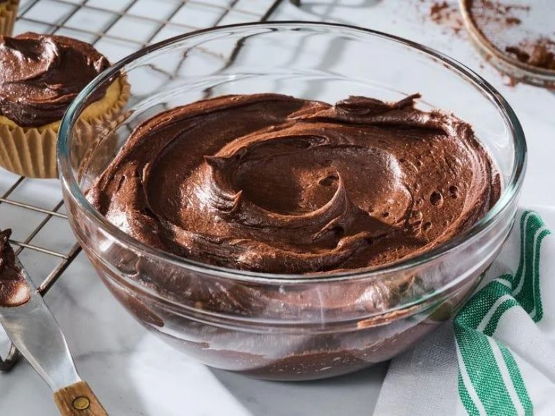 Creamy chocolate buttercream frosting with a spatula in a mixing bowl
