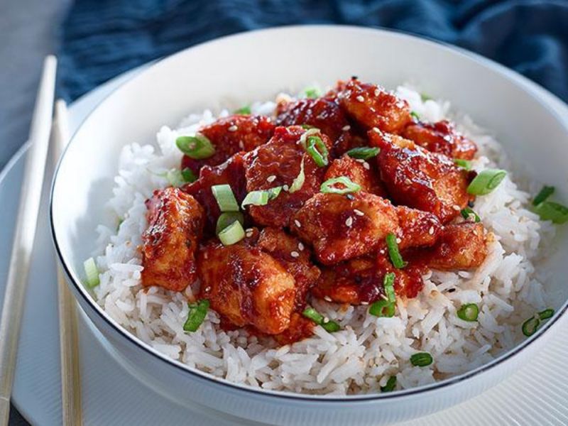 Finished sweet chilli chicken with bell peppers in sticky garlic chilli glaze, topped with sesame seeds and sliced green onions and served over basmati rice