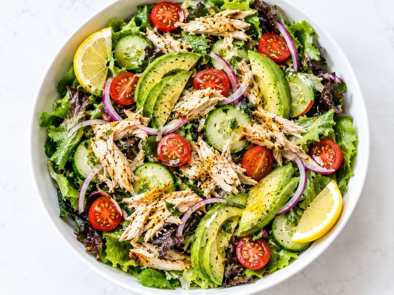 Healthy rotisserie chicken quinoa bowl with broccoli, bell peppers, beans, and avocado