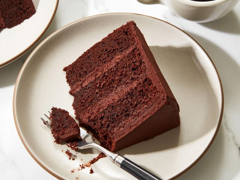 A slice of chocolate cake served on a plate with coffee